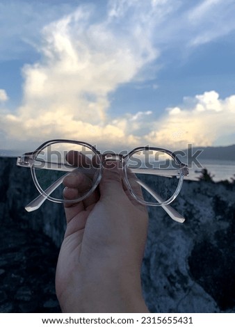 a woman taking a photo of her glasses with a natural landscape as a background on Ternate Island, North Maluku province.