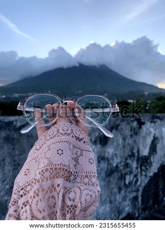 a woman taking a photo of her glasses with a natural landscape as a background on Ternate Island, North Maluku province.
