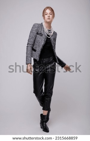Fashion photo of a beautiful elegant young woman in a pretty suit, black leather pants, trousers, gray jacket, blazer, top posing on white background. Studio Shot, portrait. Slim figure. Blonde