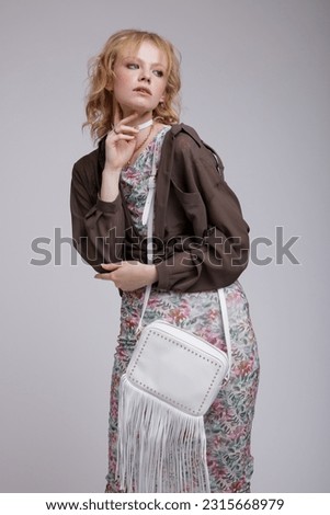 High fashion photo of beautiful elegant young woman in a pretty dress with floral pattern, green brown cardigan, choker, handbag posing over white background. Studio Shot, portrait. Blonde
