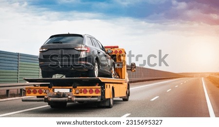 A tow truck on the public road. A tow truck with a broken car on a country road. Tow truck transporting a car on the highway. Car service transportation concept. Royalty-Free Stock Photo #2315695327