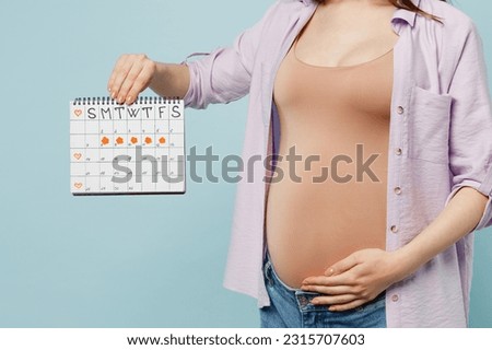 Cropped close up young pregnant future mom woman with tummy with baby wear casual clothes hold in hands calendar stroking belly isolated on plain pastel blue background. Maternity pregnancy concept