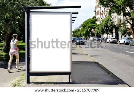 bus shelter at bus stop. white poster and commercial ad space display lightbox. mockup base. blank ad panel. glass design. urban street setting. blurred pedestrians in the background. car road traffic