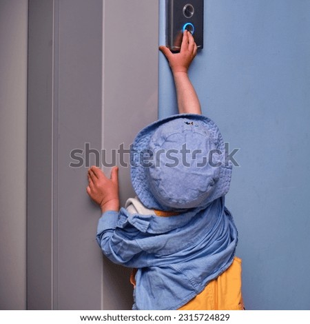 Toddler baby calls the elevator by pressing the button in the entrance hall on the floor. A child reaches for the elevator call button in an apartment building. Kid aged about two years Royalty-Free Stock Photo #2315724829