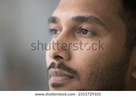 Thoughtful handsome young Indian man facial close up portrait. Face of pensive serious attractive guy with stylish stubble, beard, looking away, thinking, dreaming
