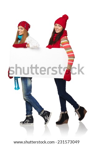 Women billboard sign. Full length of two happy women wearing winter clothing smiling carrying blank white placard, over white background