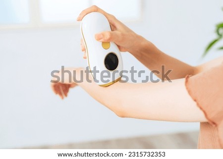 A woman using an epilator to remove unwanted arm hair at home. Royalty-Free Stock Photo #2315732353