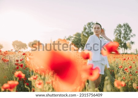 Young woman in white clothes walking and enjoying among flowering poppies meadow at sunset. Image with copy space.