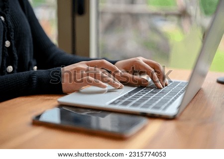 Close-up image of a woman using a laptop computer while sitting at a table by the window in the coffee shop. typing on the keyboard, browsing the internet, chatting, and responding to emails