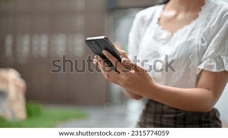 A woman in casual clothes using her smartphone, chatting with her friends while relaxing in the park. close-up image