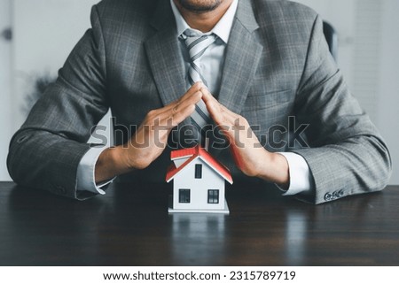 Property insurance and security concept. Protecting gesture of man and symbol of house. Estate agent giving house keys to woman and asked customer to sign the documents to make the contract legally.