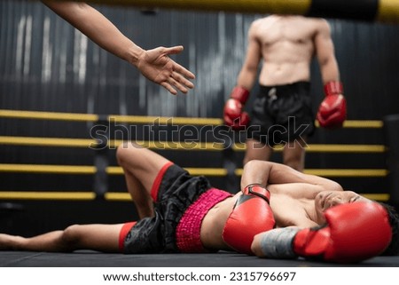 Asian boxer athlete man knocked out unconscious and laying down on floor center stage ring. Hand of referee counting down knockout. Sportsman muay Thai boxer training, work out at the gym. Royalty-Free Stock Photo #2315796697