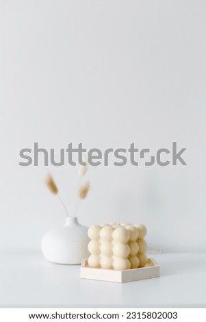 Creative composition of living room interior with copy space, stylish vase, wall with stucco.Home decor. Template. Hygge scene with candles on white background. Bunny candle. Bubbles candle
