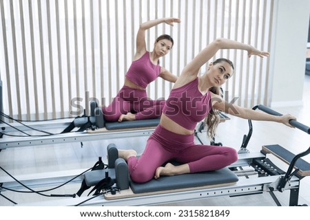 Two Asian women in pink sportswear doing side bends on a reformer machine. Pilates classes. Royalty-Free Stock Photo #2315821849