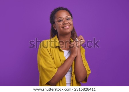 Young smiling attractive African American woman looking cutely at camera flirting with interlocutor and rubbing hands in anticipation of response dressed in casual style stands on purple background. Royalty-Free Stock Photo #2315828411