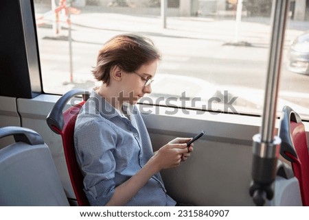 Tennager boy in a tram holding mobile phone in his hand. Guy siting near a window, looks with interest at screen of smartphone, playing mobile games online on smartphone connected to public wifi Royalty-Free Stock Photo #2315840907