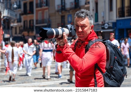 Photographer on San Fermin. Photojournalist. People celebrate San Fermin festival in traditional white and red clothing with red necktie, Pamplona, Navarra, Spain
