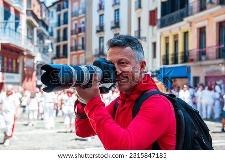 Photographer on San Fermin. Photojournalist. People celebrate San Fermin festival in traditional white and red clothing with red necktie, Pamplona, Navarra, Spain. Royalty-Free Stock Photo #2315847185