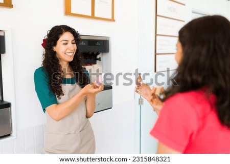 Hispanic woman in her 20s working at the gelato shop giving free ice cream or frozen yogurt samples to the teen girls  Royalty-Free Stock Photo #2315848321