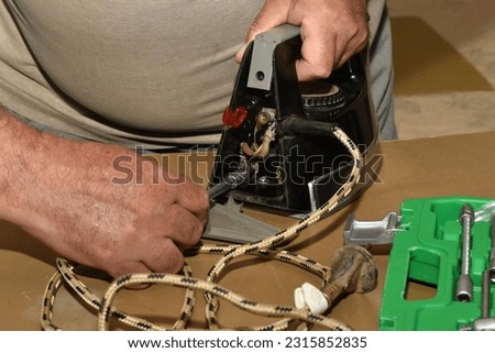 In the picture of the hand of a man who is busy repairing the iron, he unscrews the bolt connecting the electric cable to the iron.