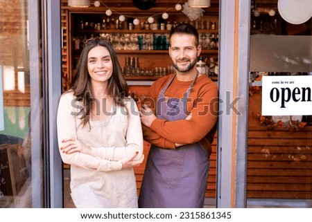Small business owner woman and man standing at the café door waiting for customers. Small business owners looking at camera and smiling.