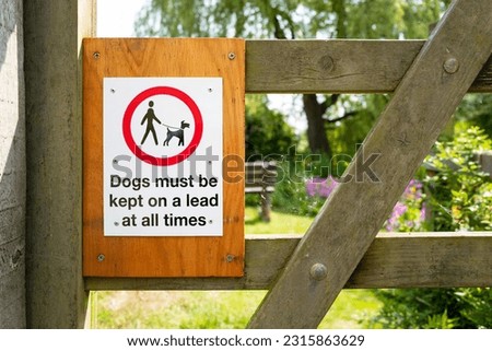 Dogs must be kept on lead sign seen attached to a garden gate leading to a secrete garden located at an old English churchyard.