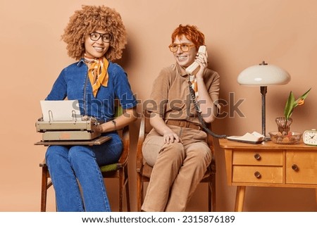 Two women dressed in old fashionable clothes diligently go about their tasks. One works on typewriter creating rhythmic clicks while other engages in phone call using stationary telephone. Retro style Royalty-Free Stock Photo #2315876189