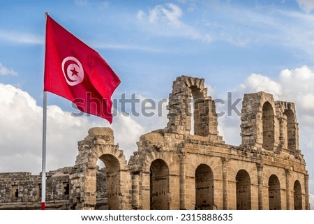 The Tunisian flag in front of the ruins of the Roman Empire amphitheater of El Jem in Tunisia. Royalty-Free Stock Photo #2315888635