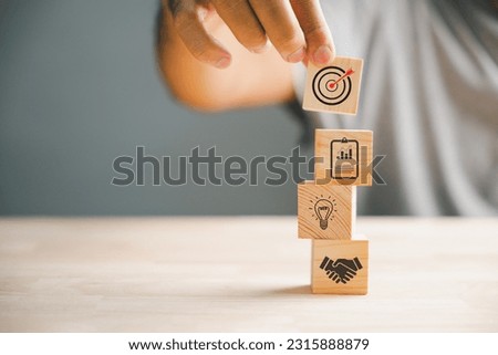 Businessman's hand skillfully arranging wood blocks, representing the icon of a business strategy and Action plan. Ample copy space for customized content. Royalty-Free Stock Photo #2315888879