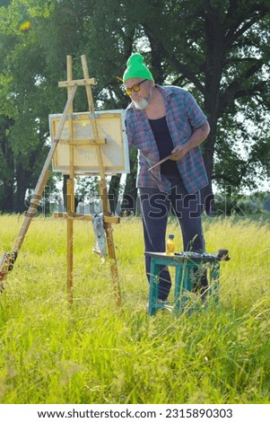 Vertical shot offbeat middle-aged bearded man artist creating picture oil painting at scenic landscape view in golden sunshine morning. Wonderful nature place of work talented painter in his maturity