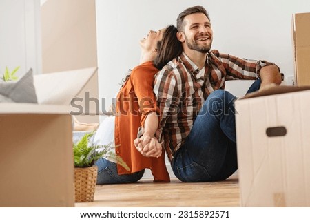 A young happy married couple expecting a baby sitting on the floor of their new home after moving in. Unpacking after relocation. New homeowners. New beginnings Royalty-Free Stock Photo #2315892571