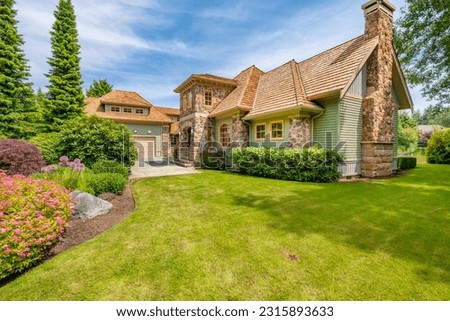 Large stately home exterior with extensive stone cladding brick chimney cedar shake roof on lush landscaping paved driveway blue sky estate house Royalty-Free Stock Photo #2315893633