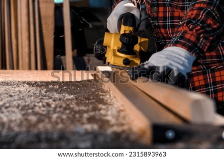 Carpenter craftsman using electric hand wood planer making pool cue or snooker cue in carpentry workplace in an old wooden shed. Handmade craftsman concept. Selective focus on wood planing. Royalty-Free Stock Photo #2315893963
