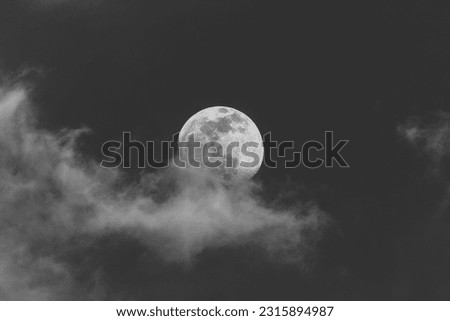 Black and white photo of the moon with whimsical fluffy clouds. Sonoran Desert sky near dusk.