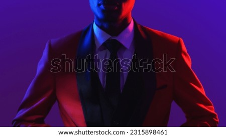 Gentleman fashion. Dandy style. Party look. Neon light unrecognizable confident man in red elegant tuxedo suit on dark fluorescent purple color background. Royalty-Free Stock Photo #2315898461