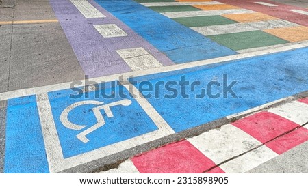 White and Blue painted handicapped sign traffic symbol on the floor in front of road for support wheelchair and colorful crosswalks.