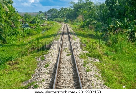 Photos from the last carriage of the train in Malaysia with blue sky in the background, green grass and crossing an iron bridge.