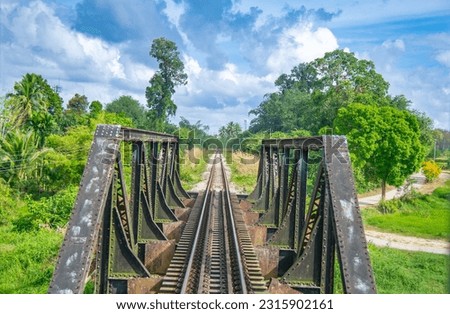 Photos from the last carriage of the train in Malaysia with blue sky in the background, green grass and crossing an iron bridge.