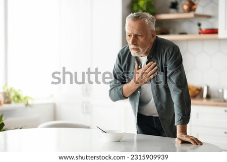 Heart Attack. Senior man suffering from chest pain at home, elderly gentleman having cardiac illness, feeling unwell, standing at table in kitchen interior and rubbing thorax area, copy space Royalty-Free Stock Photo #2315909939