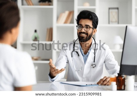 Young arab man doctor consulting lady patient, filling form at consultation. Handsome bearded family doctor man wearing white coat talking to woman while appointment visit in modern clinic Royalty-Free Stock Photo #2315909981