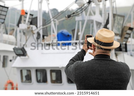 elderly person taking pictures with a mobile phone of a getaria fishing boat