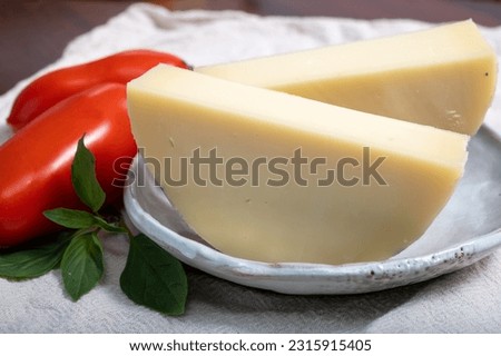 Italian cheese, Provolone dolce cow cheese from Cremona served with olive bread and tomatoes close up. Royalty-Free Stock Photo #2315915405