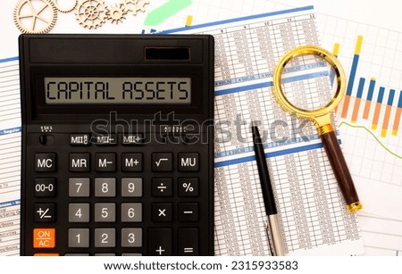 Calculator, multi-colored paper clips and a white card with the inscription ASSETS on a light wooden table. Stationery and calculator.