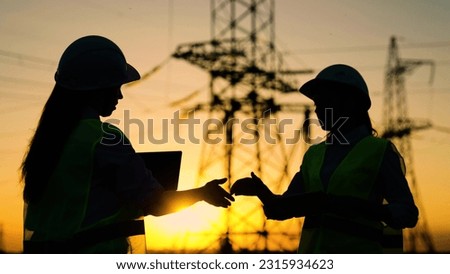 Colleagues women shake hands. Teamwork of power engineers in protective helmets, maintenance of power lines in outdoors. Two construction engineers work together on an electrical transmission line. Royalty-Free Stock Photo #2315934623