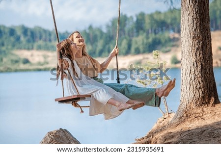 Mom swings with her daughter on a rope swing against the backdrop of a forest lake reflecting sky. Family concept