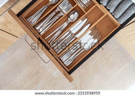 Top view of cutlery set in bamboo trays in kitchen drawer. Keeping steel spoons, knives, forks and other utensilin organizer box with minimalist order. Modern storage idea Royalty-Free Stock Photo #2315938959
