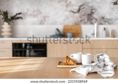 homemade croissant and cups of coffee on bamboo tray near striped towel from cotton material on wood tabletop on blurred kitchen background