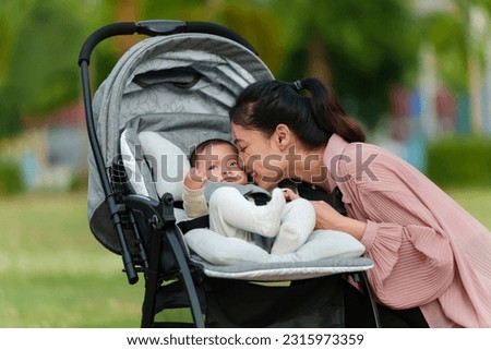 mother kissing with her infant baby in the stroller while resting in the park