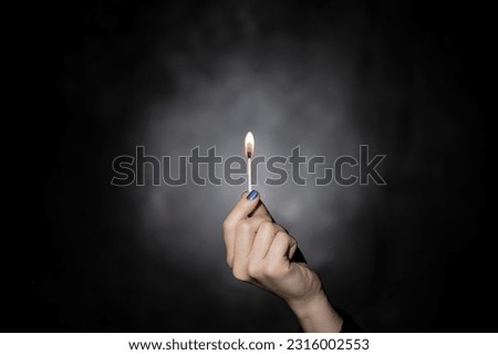 Woman's hand holding lit match on black background. Royalty-Free Stock Photo #2316002553