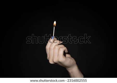 Woman's hand holding lit match on black background. Royalty-Free Stock Photo #2316002555